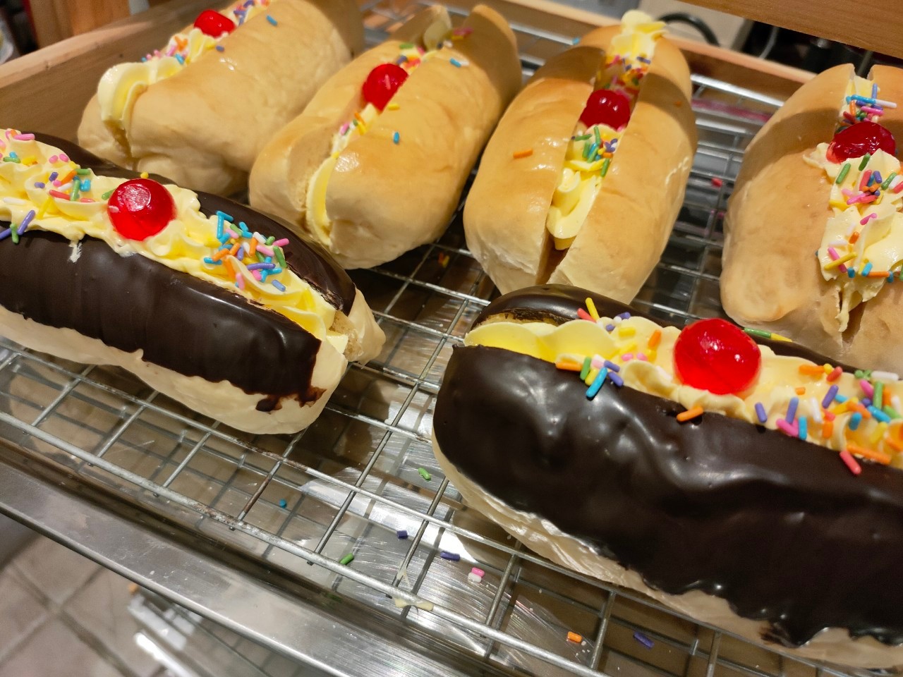 ขนมปังฮอทดอกโบราณสอดไส้บัตเตอร์ครีมตกแต่งด้วยเยลลี่เชอร์รี่และเกล็ดน้ำตาล และมีแบบชุบชอคโกแลต