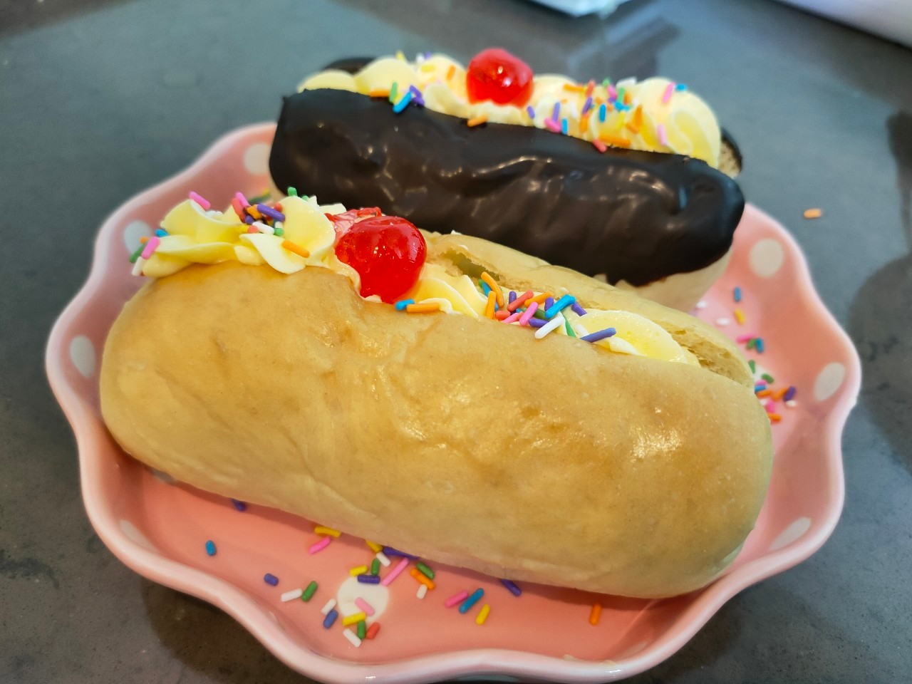 ขนมปังฮอทดอกโบราณสอดไส้บัตเตอร์ครีมตกแต่งด้วยเยลลี่เชอร์รี่และเกล็ดน้ำตาล และมีแบบชุบชอคโกแลต