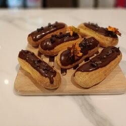 เอแคลย์ไส้ครีมสดรสชอคโกแลต ตกแต่งด้วยชอคโกแลตกานาซและโกโก้นิป ดอกไม้ทานได้ ขนาดยาวประมาณ 8-9ซม ต่อชิ้น